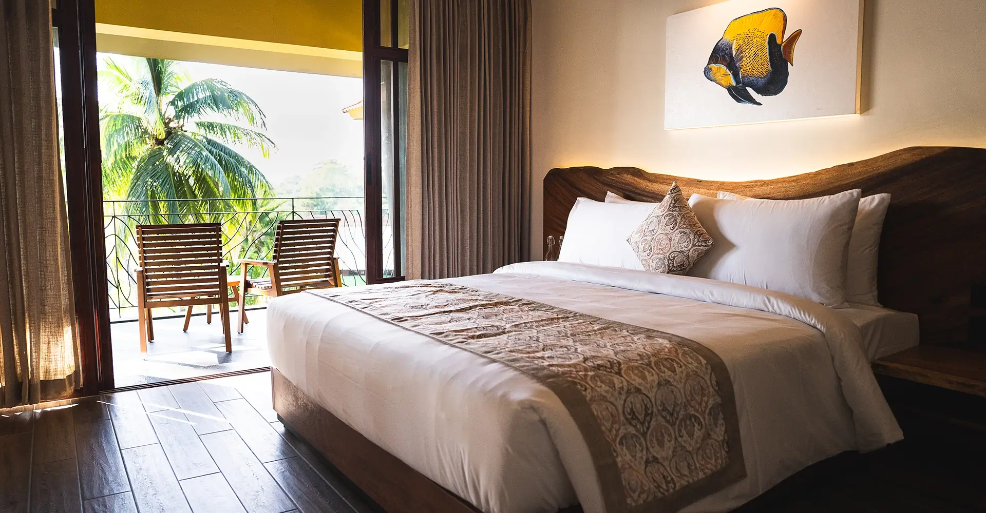 Luxury bedroom at Waterwoods Havelock with balcony view of lush coconut trees and wooden furniture.