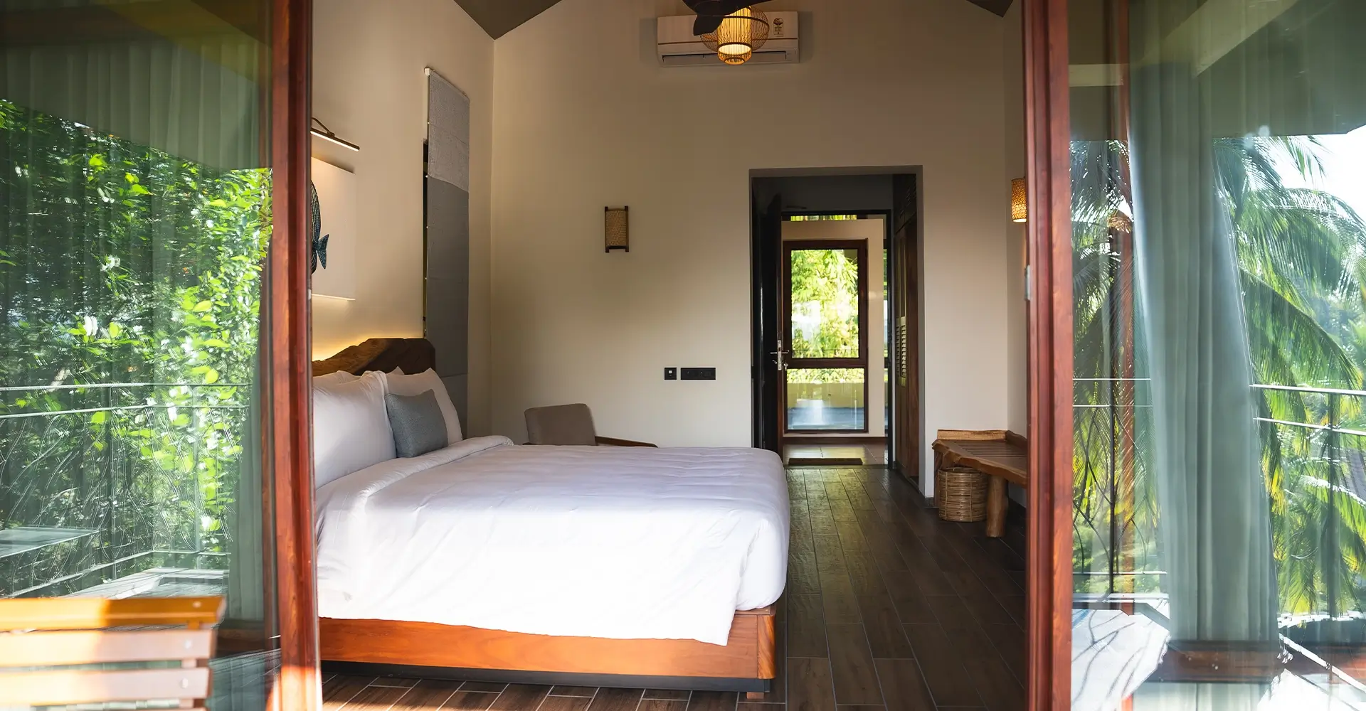 Spacious bedroom at Waterwoods Havelock with glass doors opening to views of coconut trees and tropical greenery.