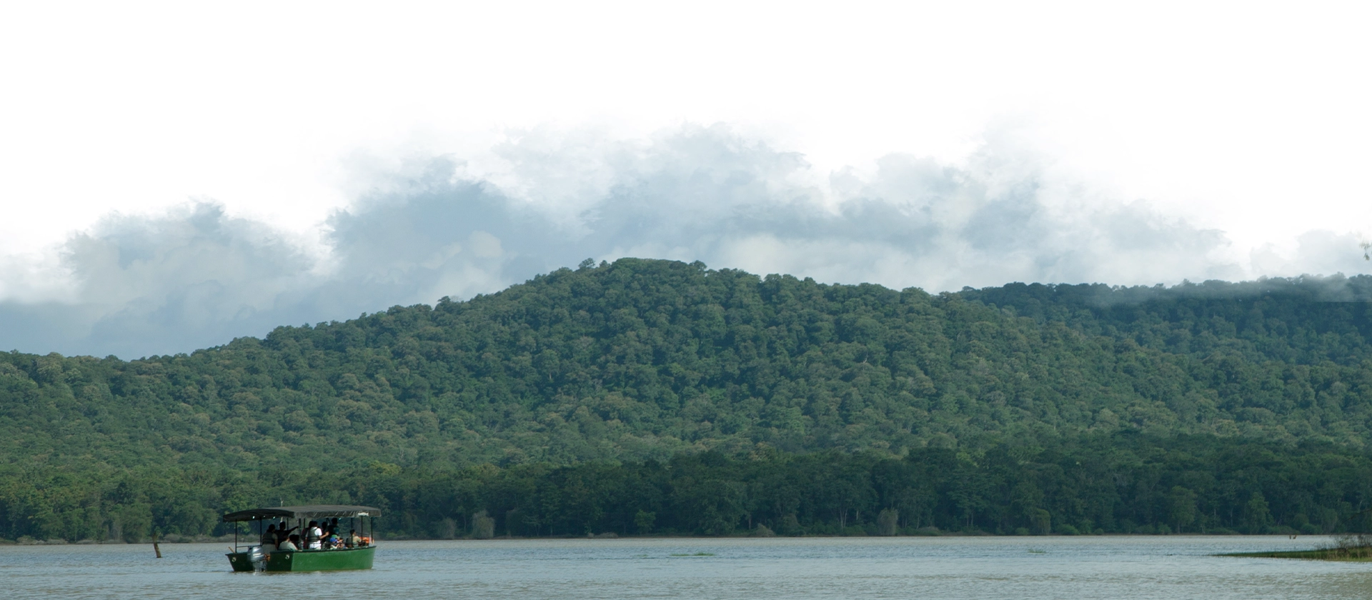 Boat safari on the Kabini River with dense forest and misty hills in the background