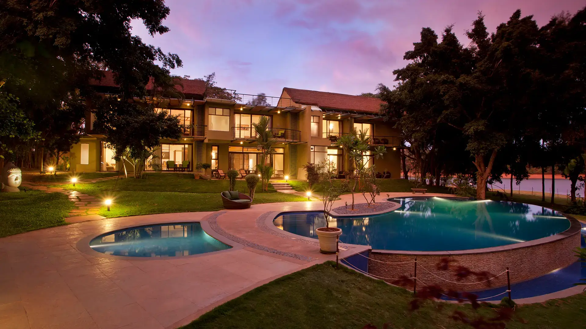 Waterwoods Kabini Lodge at sunset with illuminated infinity pool and surrounding greenery