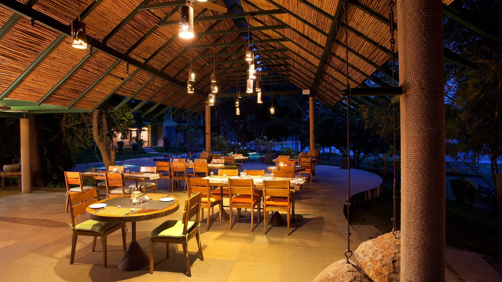 Open-air riverside dining area illuminated with warm lights at Waterwoods Kabini