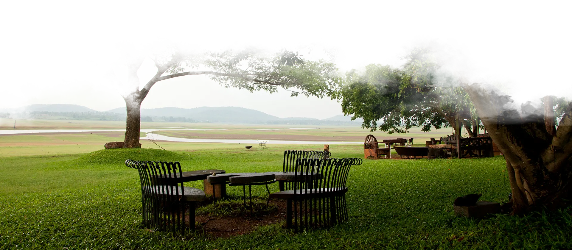 Outdoor seating area overlooking Kabini backwaters at Waterwoods Lodge with misty hills in the background.